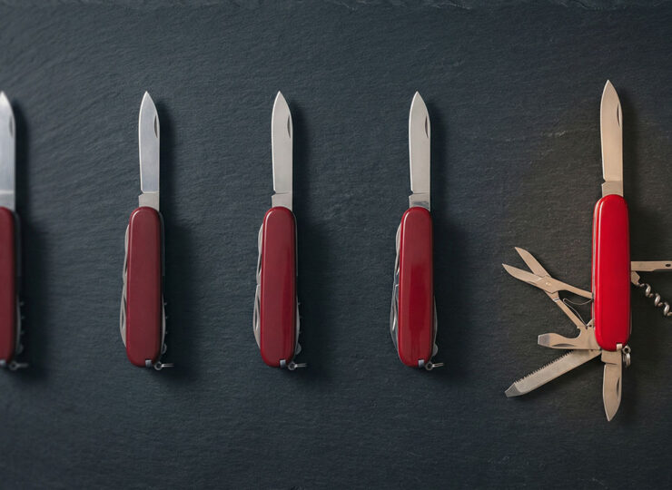 Row of identical Swiss Army knives each with only one blade open, next to a single knife with multiple different tools extended
